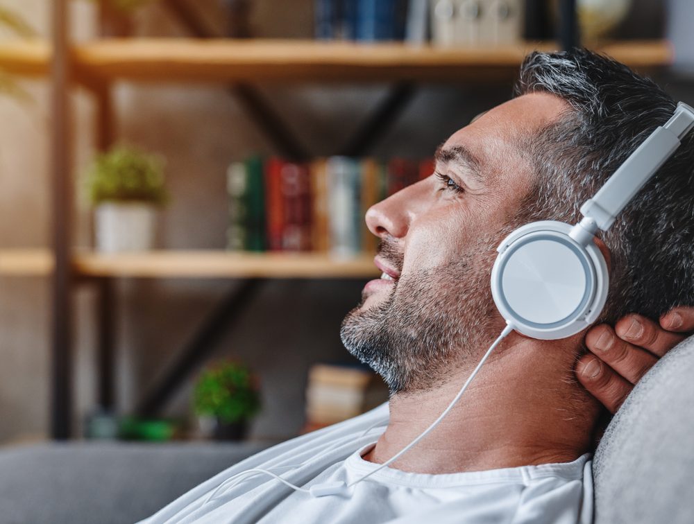 A man relaxing on the couch, listening to an audiobook through headphones