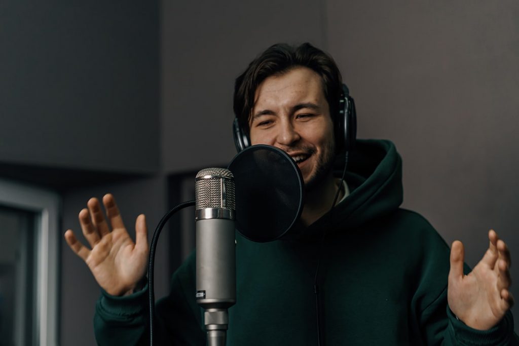 Uśmiechnięta postać lektora przed mikrofonem czytający z emocjami tekst reklamy